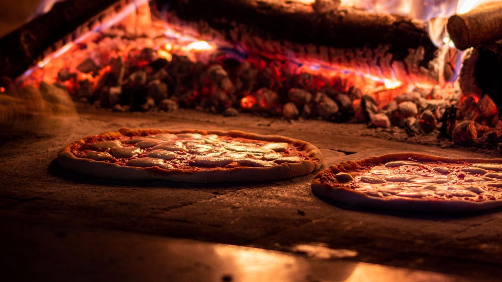 Pizzas assando no forno a lenha, com a brasa ao fundo